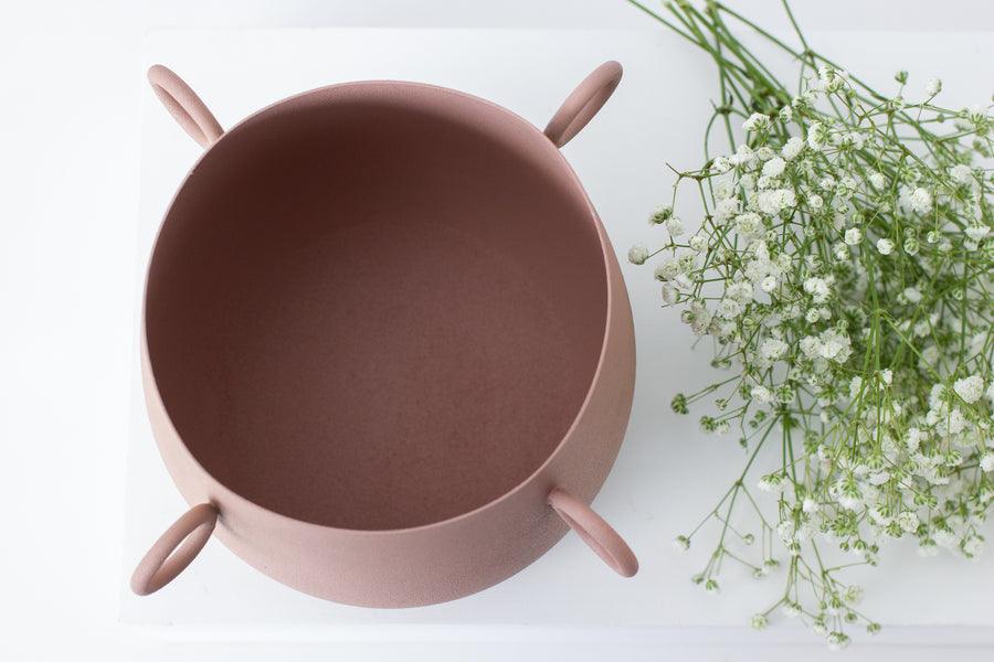 The Pale Pink coloured Sedona Pot is a made of iron and has three small circle handles. Lightweight, with a fine textured surface. From our range of small pots, the Sedona pot is ideal for indoor use with living and faux plants. Do not plant directly into the vessel.